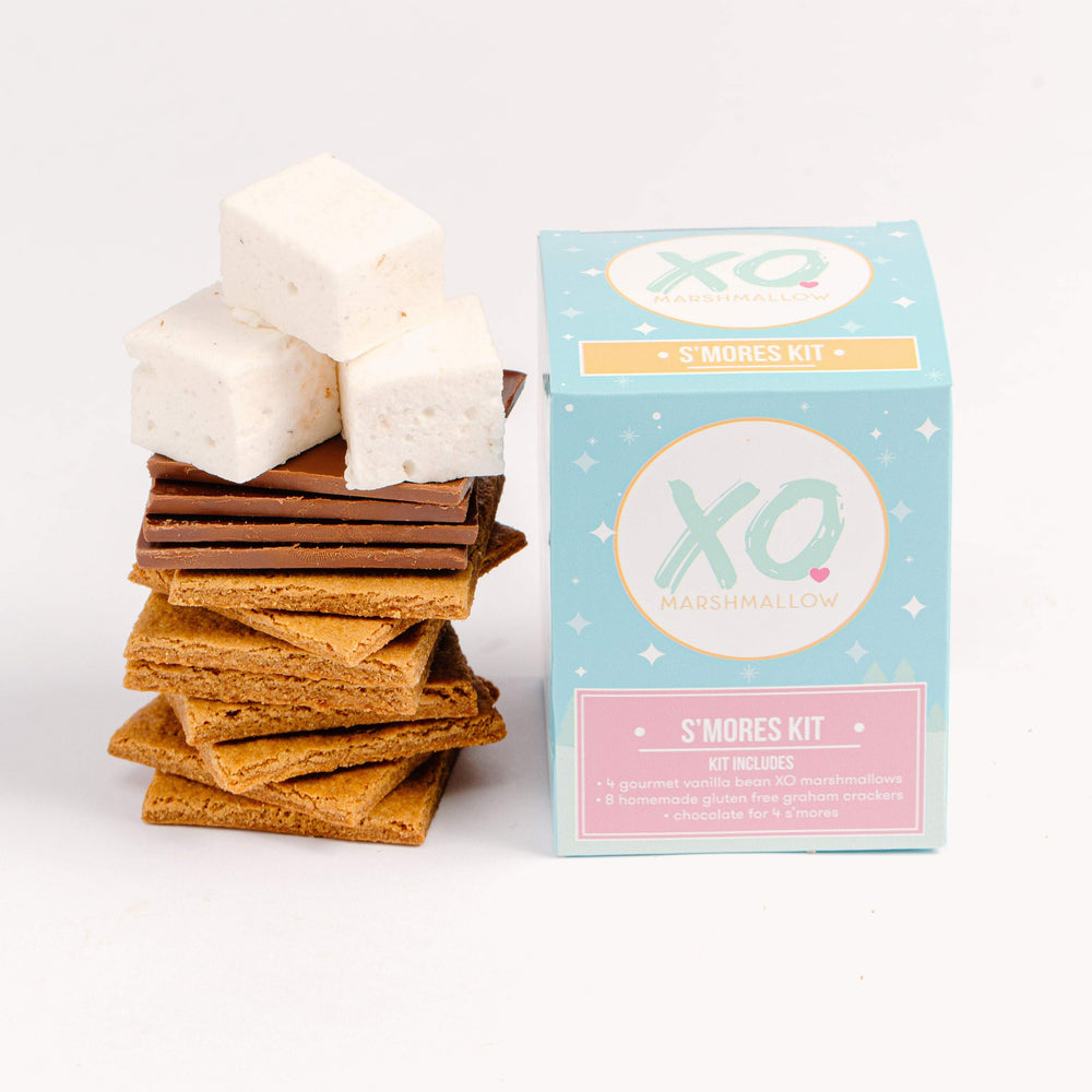 A stack of gluten free graham crackers, chocolate bars, and vanilla marshmallows next to a box called XO Marshmallow S'mores Kit