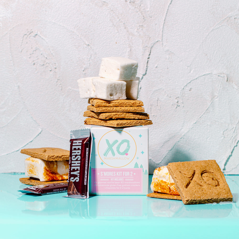 XO Marshmallow's s'mores kit for 2 packaging with all of the s'mores products around it against a white textured background.